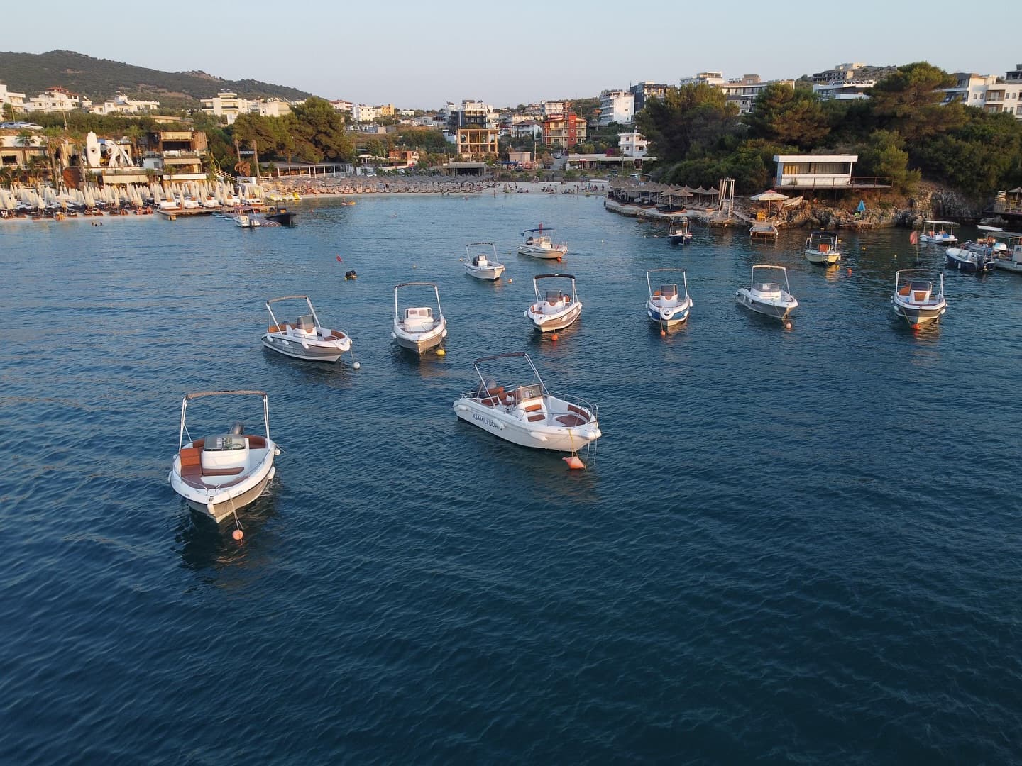 Aerial view of the Ksamili Boats fleet moored along the Rruga Riviera waterfront at golden hour